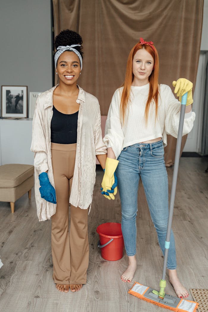 about-01 Two women smiling and holding hands while cleaning indoors, symbolizing teamwork.